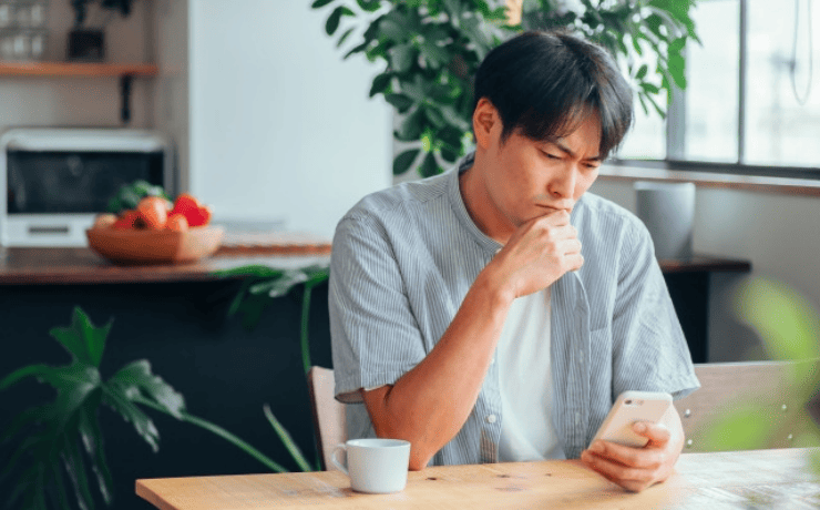 スマホ画面を見て悩む男性