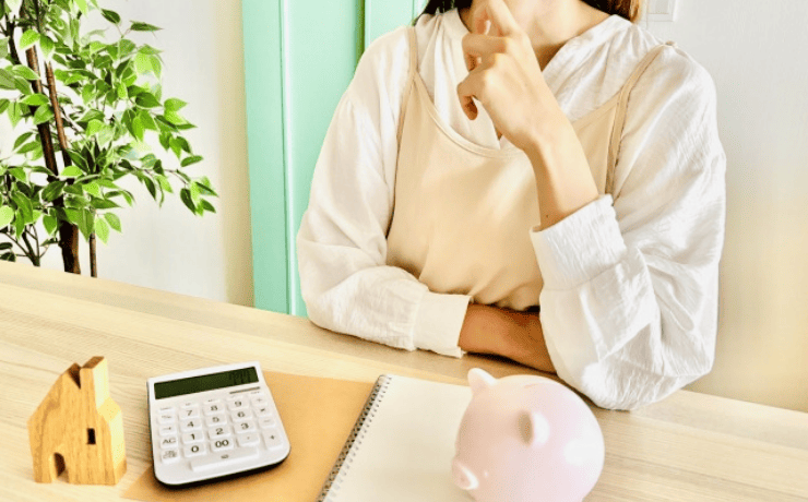 電卓と貯金箱の前で悩む女性