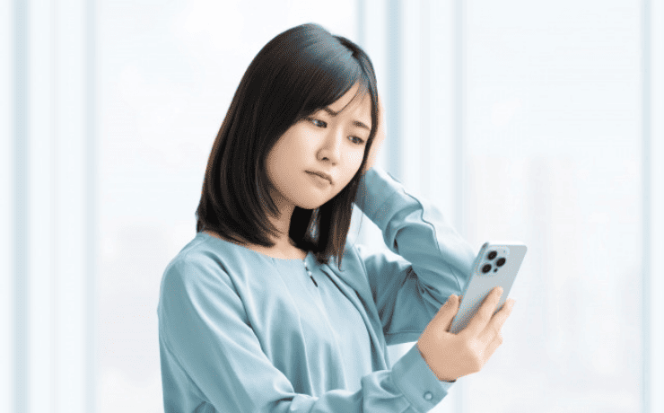 スマホ画面を見て悩む女性