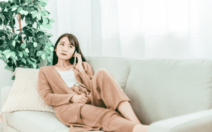 ソファに寝そべりスマホで通話する女性