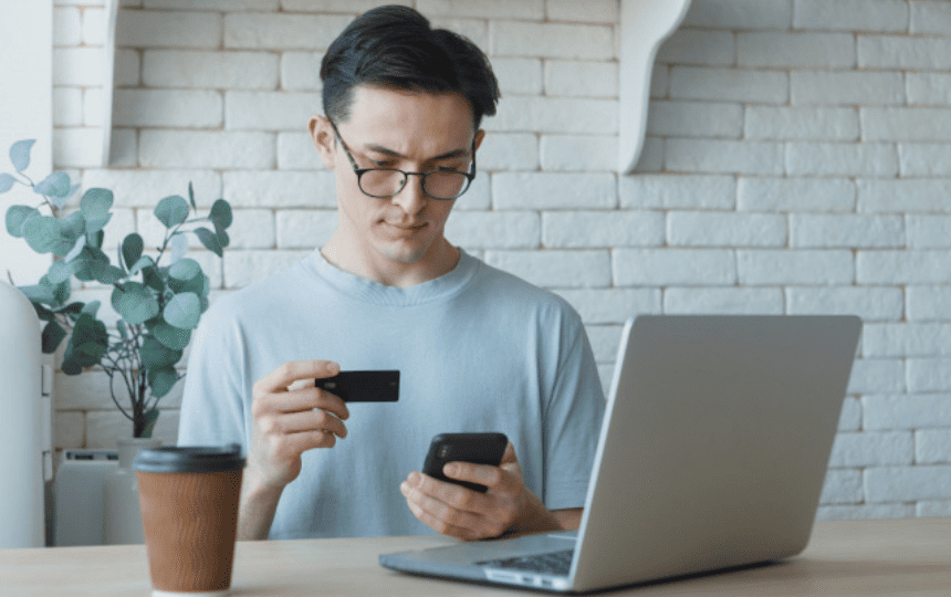 スマホとクレカを見比べる、パソコンの前に座る男性