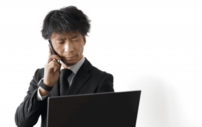 パソコンを見ながらスマホで電話するスーツ姿の男性