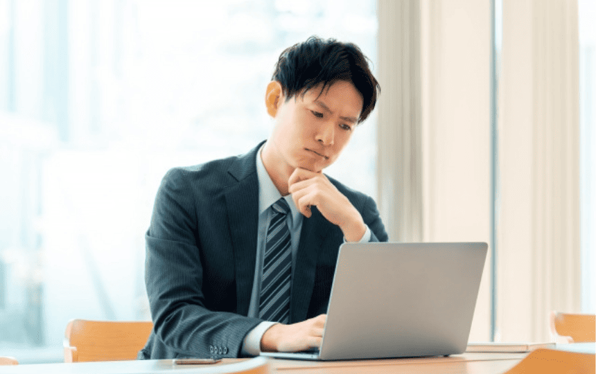 難しい顔でノートパソコンを操作するスーツ姿の男性