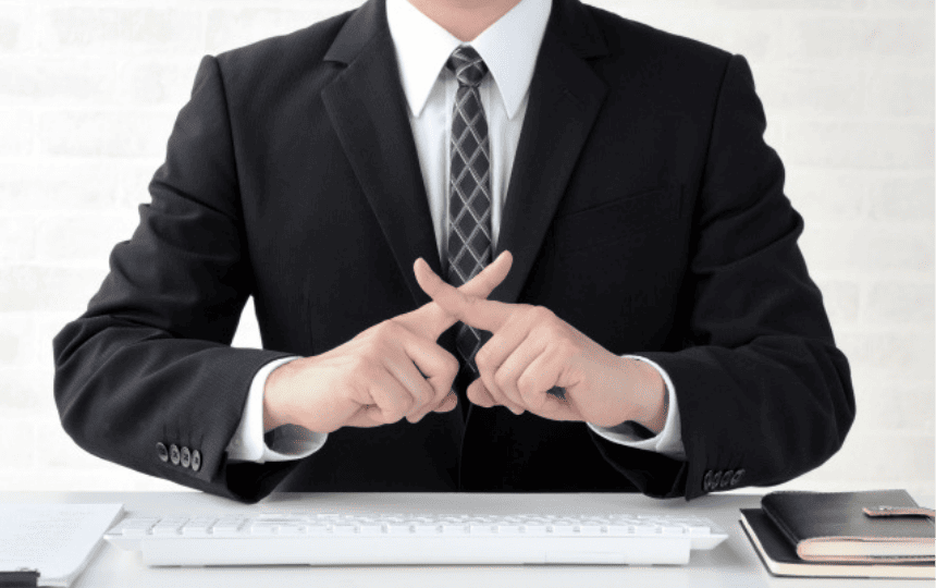 指でばつ印を掲げるスーツ姿の男性