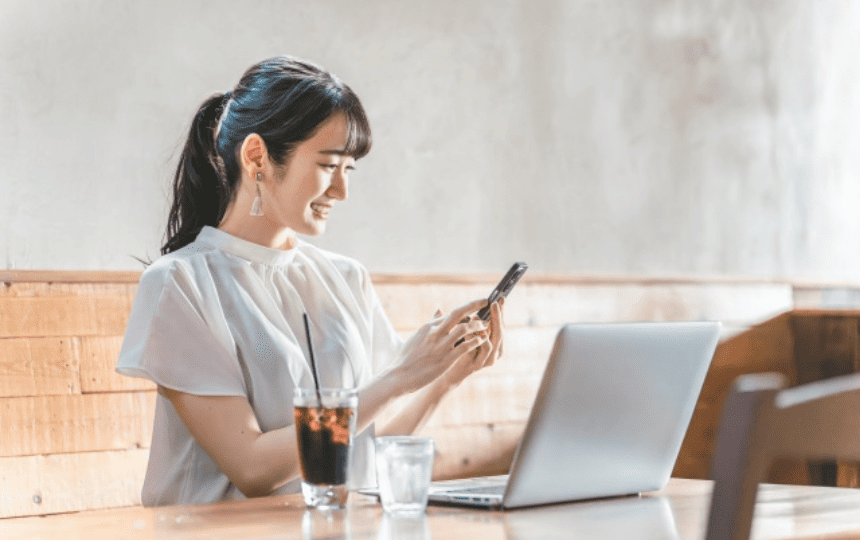 スマホを持ちノートパソコンの前で笑顔の女性