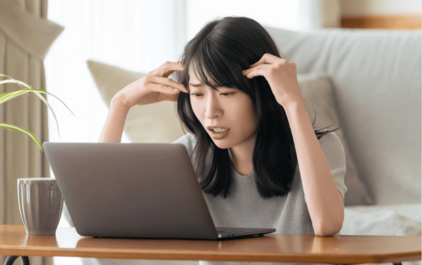 頭を抱えて悩む女性がノートパソコンを見ている様子