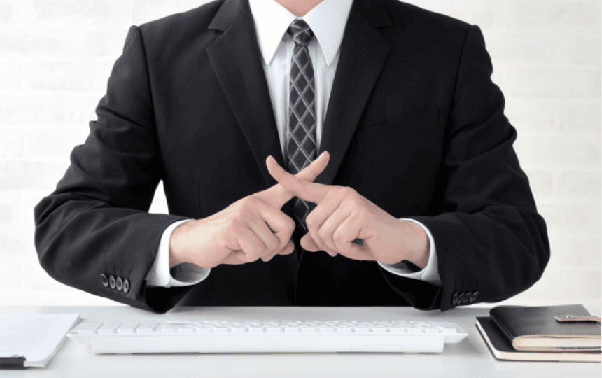 指でばつ印を作るスーツ姿の男性