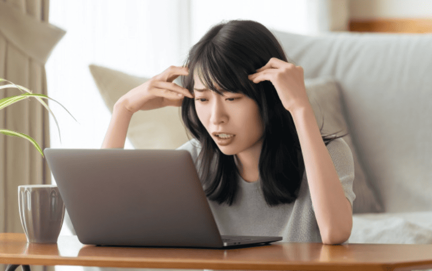 頭を抱えてノートパソコンを見る女性