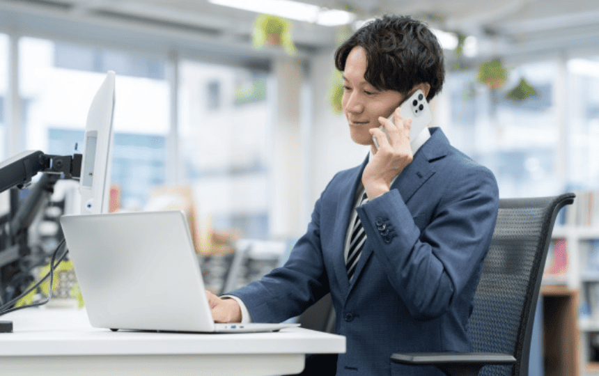 スマホで通話しながらノートパソコンを操作する男性