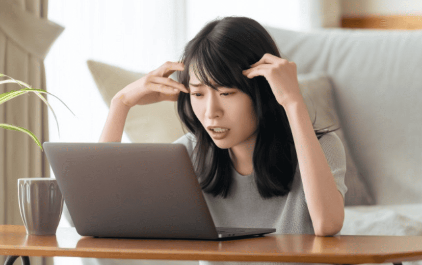 頭を抱えてノートパソコンを見る女性