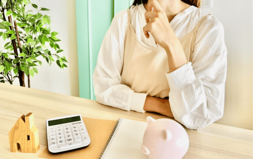 貯金箱と電卓の前に座る女性