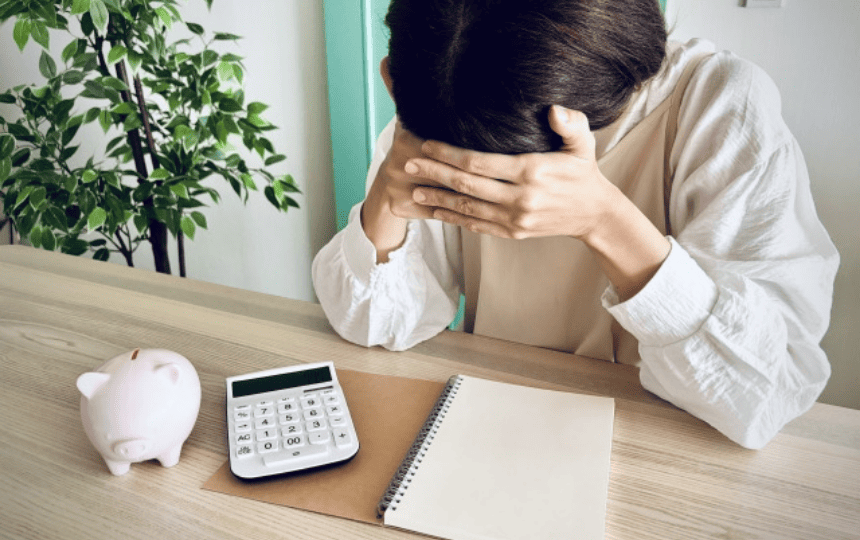 豚の貯金箱と電卓を前に頭をかかえる女性